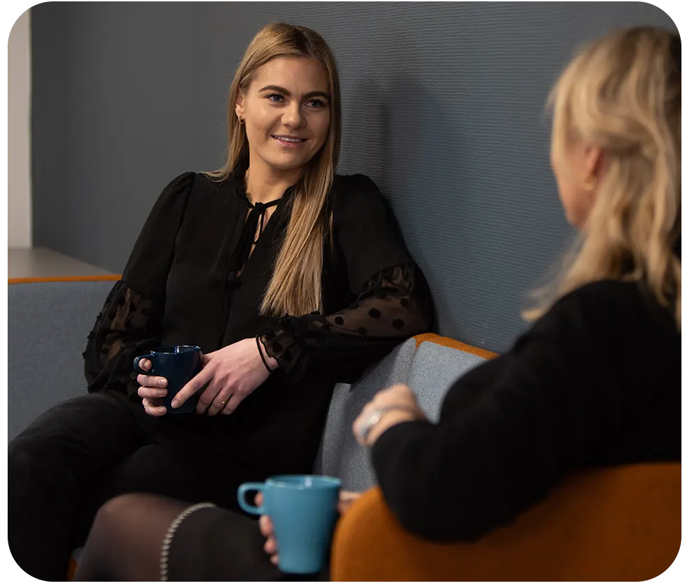 To kvinner som sitter i en sofa og diskuterer lønn.